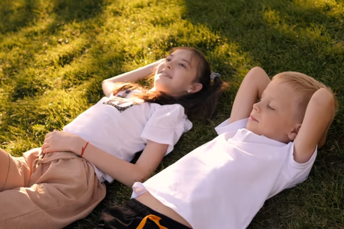 Des enfants souriants jouent dans l'herbe devant un gîte familial dans les Vosges.